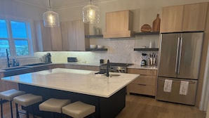 Una cocina moderna con una isla grande, taburetes de bar, electrodomésticos de acero inoxidable e iluminación colgante.