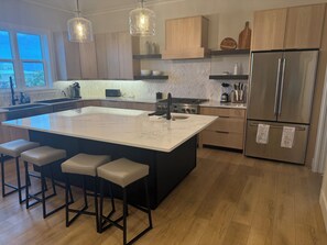 A modern kitchen with a large island, bar stools, stainless steel appliances, and pendant lighting. - Spacious Custom New 5-bedroom house, Sleeps 12, Private Dock, Elevator (Englewood)