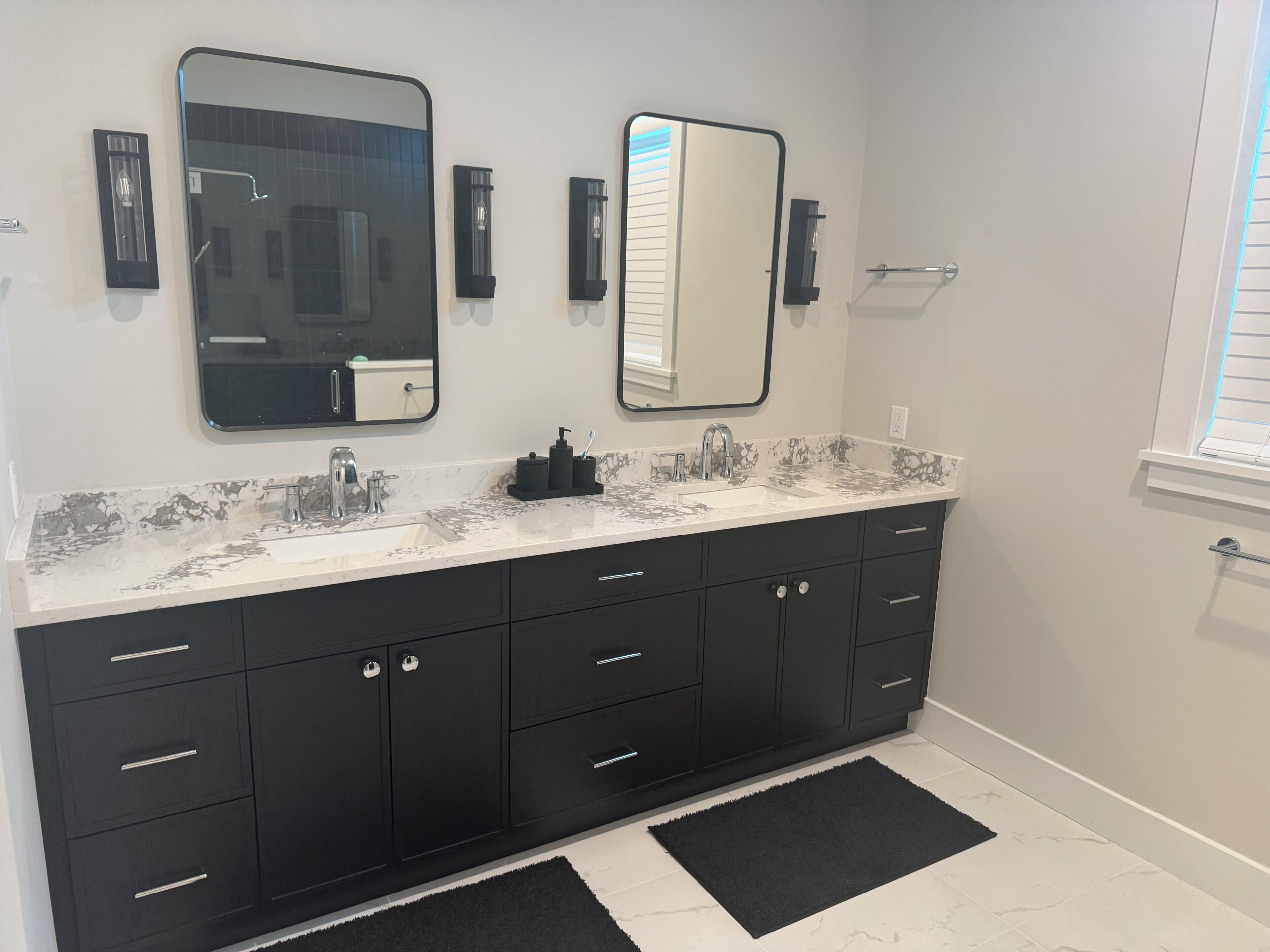 Un baño moderno con tocador de doble lavabo, muebles negros y encimera de mármol.