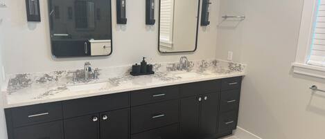 Un baño moderno con tocador de doble lavabo, muebles negros y encimera de mármol.