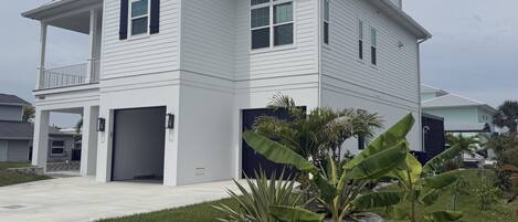 A two-story house with a covered porch, a garage, and a well-maintained lawn with tropical plants.