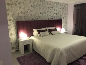 Een slaapkamer met een groot bed, twee nachtkastjes met lampen, bloemenbehang en een paars tapijt.