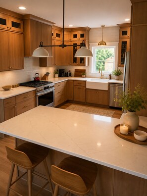 A modern kitchen with wooden cabinets, a central island, bar stools, and pendant lighting. - Collins River Farmhouse (McMinnville)