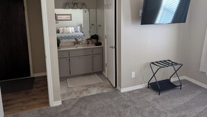Une chambre à coucher comprenant un lit, une commode, un miroir, un téléviseur et un petit coin salon.