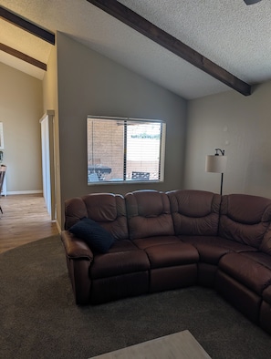 A living room with a brown sectional sofa, a lamp, and a window with blinds. - Beautiful 2-bedroom townhome on golf course in Mesa (mesa)