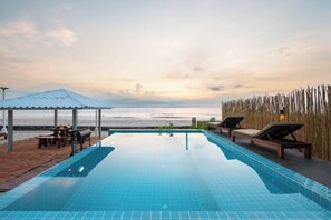 Ein klarer Blick auf einen Swimmingpool mit Liegestühlen und einer überdachten Sitzgelegenheit mit Blick auf den Strand.