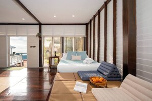 Ein Schlafzimmer mit einem Bett, einem Sofa, einem kleinen Tisch mit Orangen und Blick ins Freie.