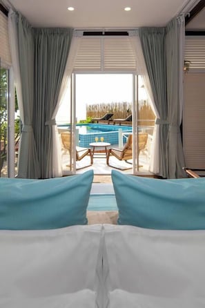 Ein Zimmer mit einem Bett, Vorhängen und Blick auf Pool und Liegestühle.