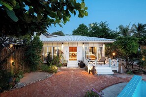 Ein Haus mit überdachter Terrasse, einem Swimmingpool und üppiger Bepflanzung.