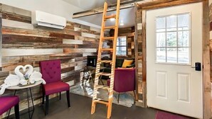 Quarto com painel de parede de madeira, escada, porta com janela e mesa com cadeiras.