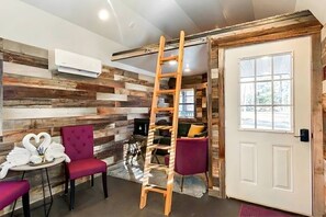 Quarto com painel de parede de madeira, escada, porta com janela e mesa com cadeiras.