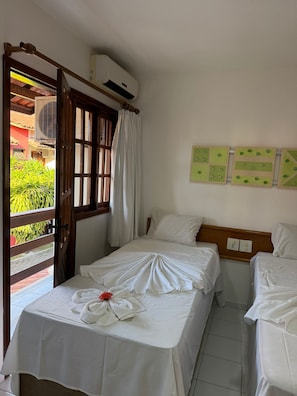 Habitación de hotel con dos camas, un equipo de aire acondicionado, una ventana con cortinas y vistas a zonas verdes.