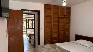 Une chambre à coucher comprenant un lit, une armoire en bois, un ventilateur de plafond et un téléviseur.