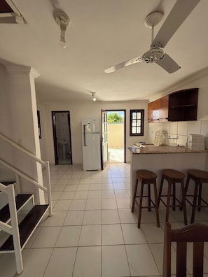 Eine Küche mit Deckenventilator, Kühlschrank, Spüle und einer Bar mit Hockern.