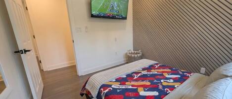 Een slaapkamer met een bed, een aan de muur bevestigde televisie, een deur en een muur met een diagonaal patroon.