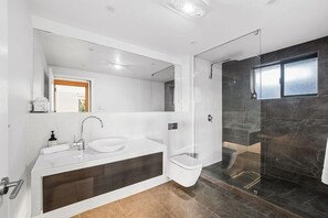 Et moderne badeværelse med vask, badekar, toilet og bruseområde med glasvægge.