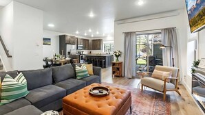 Una sala moderna con un sofá gris, un otomano marrón y un sillón color beige.