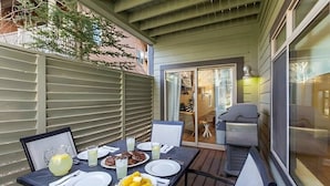 Un patio exterior con una mesa lista para comer, una parrilla y un ventanal corredizo que da a un espacio interior.
