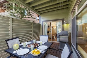 Een terras buiten met een eettafel, een barbecue en een schuifpui die naar een binnenruimte leidt.