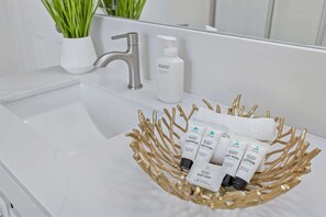 Une salle de bain avec un lavabo blanc, un robinet argenté et un panier décoratif en feuille d’or contenant des articles de toilette.