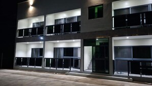 En bygning med flere etager, altaner, store vinduer og en godt oplyst indgang.