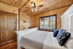 Ein Schlafzimmer in einer Holzhütte mit einem Bett, einem Deckenventilator und einem Fenster.