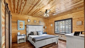 Une chambre aux murs lambrissés, avec un lit, des tables de chevet, un ventilateur de plafond et une fenêtre.