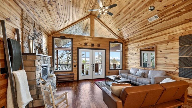 L’intérieur d’une cabane en rondins, avec une cheminée en pierre, un plancher en bois, un canapé et un ventilateur de plafond.