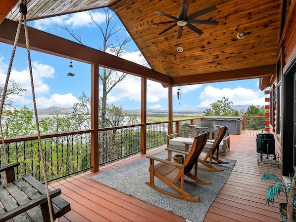 A wooden deck with a ceiling fan, a table with chairs, and a grill.