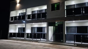 A multi-story building with balconies, large windows, and a well-lit entrance. - Pacific Sunrise Apartments #4 (Western Division)