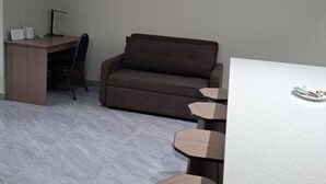 A room with a desk, chair, sofa, and a table with stools. - Pacific Sunrise Apartments #4 (Western Division)