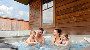 Una familia en un jacuzzi con paredes de madera y una ventana.