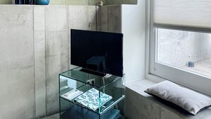 A modern room with a TV on a glass stand, a window with a view, and a concrete wall. - Studio Margriet - coming home to Bergen (Bergen)