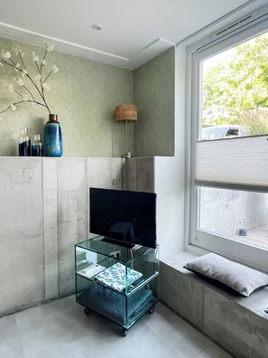 A modern room with a TV on a glass stand, a window with a view, and a concrete wall. - Studio Margriet - coming home to Bergen (Bergen)