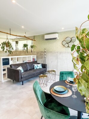 A modern living room with a sofa, a dining table with chairs, and hanging plants. - Studio Margriet - coming home to Bergen (Bergen)