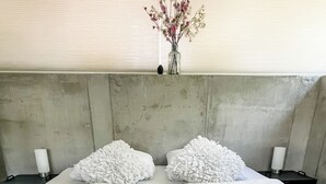 A hotel room with two beds, white linens, a vase with flowers, and a concrete headboard. - Studio Margriet - coming home to Bergen (Bergen)