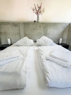 A hotel room with two beds, white linens, a vase with flowers, and a concrete headboard. - Studio Margriet - coming home to Bergen (Bergen)