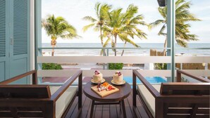 Un balcón con vistas al océano, palmeras y una mesa con dos pasteles y fruta.