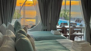 Un dormitorio con una cama grande, vista al océano y un área de piscina visible a través de la ventana.