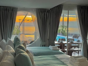 Ein Schlafzimmer mit einem großen Bett, Blick auf den Ozean und Poolanlage, die durch das Fenster sichtbar ist.