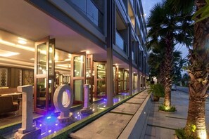 Ein modernes Hotel mit Glasfassade, Wasserspiel und Palmen.