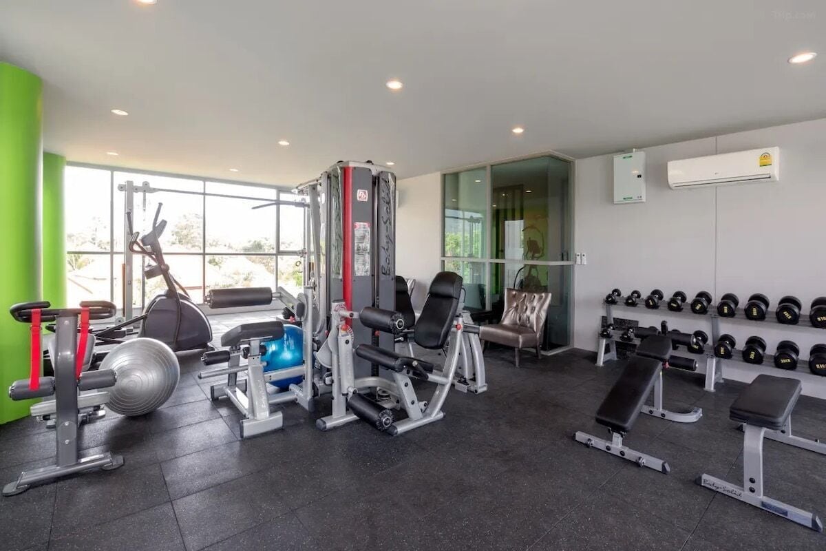 Un gimnasio con equipamiento de ejercicio, bancos y una pared llena de mancuernas.