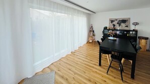 Una stanza spaziosa con un'ampia finestra, un pavimento in legno, un tavolo da pranzo con sedie e una mappa del mondo appesa al muro.