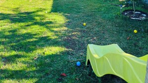 Un giardino con prato, una tenda gialla da gioco e una casa con tetto in tegole.