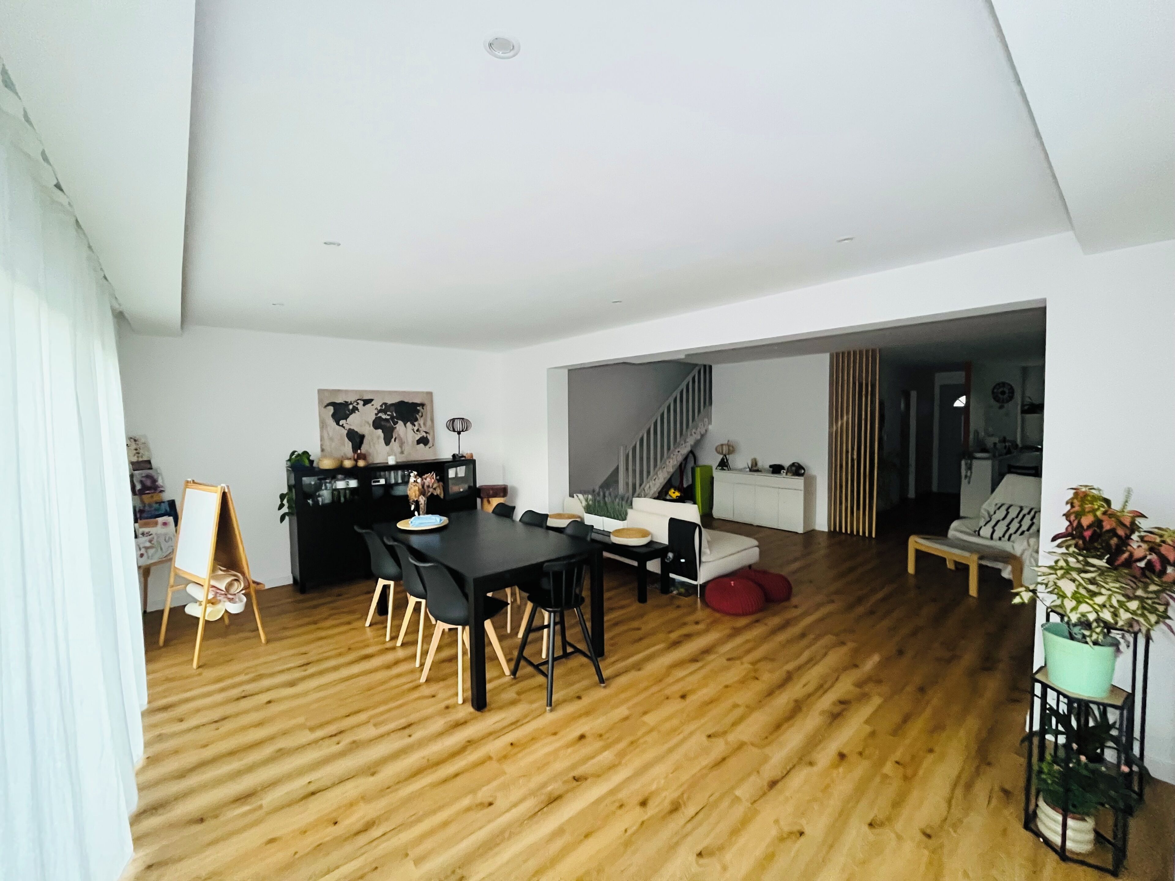 Un salon moderne avec un plancher en bois, un coin repas avec une table et des chaises noires, un escalier et une vue sur une autre pièce.
