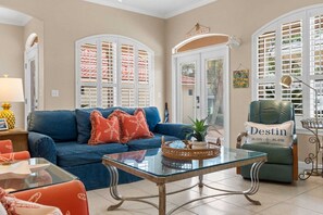 Ein Wohnzimmer mit einem blauen Sofa, einem Glastisch und einem grünen Sessel mit der Aufschrift 'Destin'.