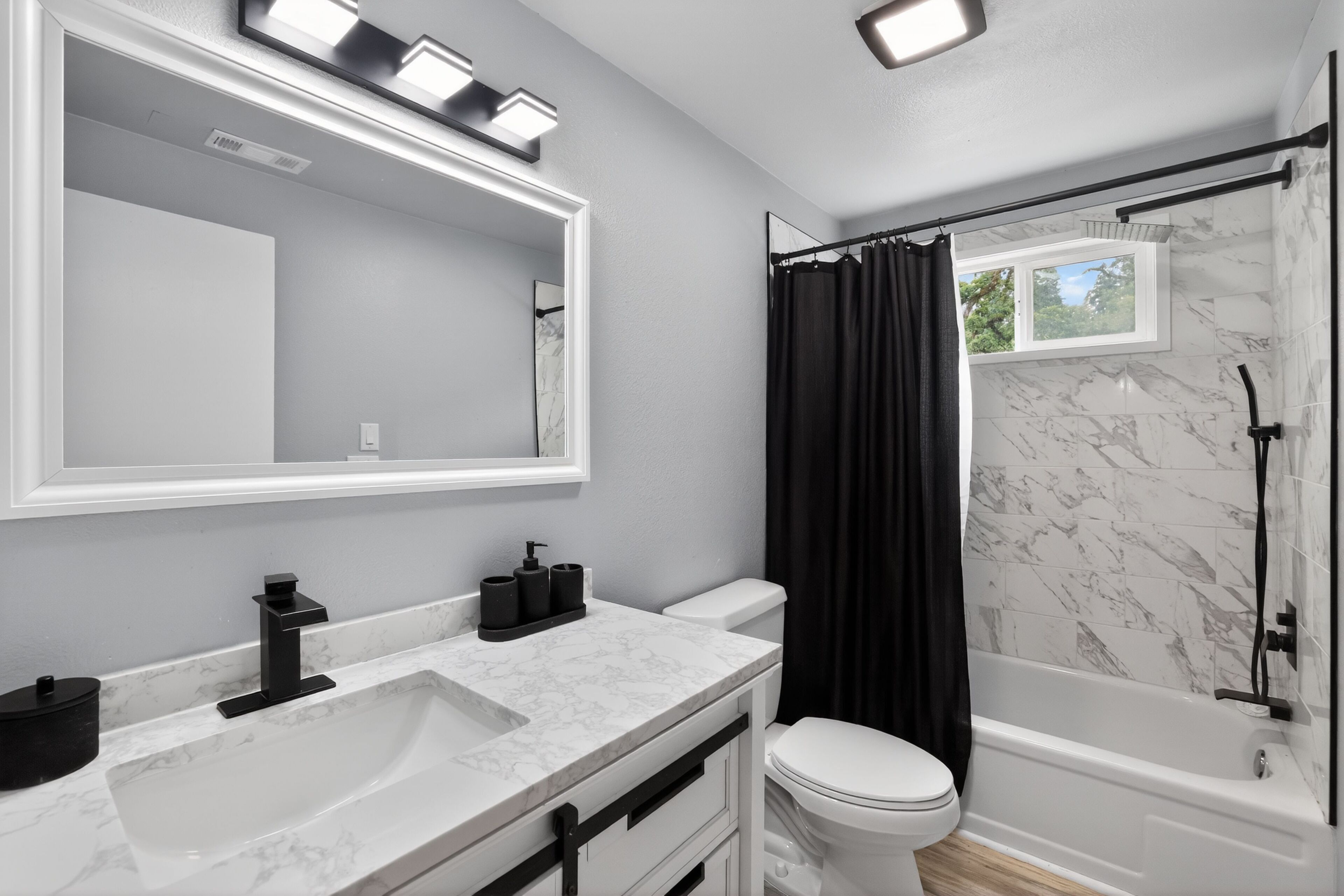 Un baño moderno con un espejo grande, un lavamanos blanco, un inodoro y una bañera.