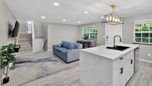 A modern kitchen with a marble island, a blue sofa, and a staircase leading to another room.