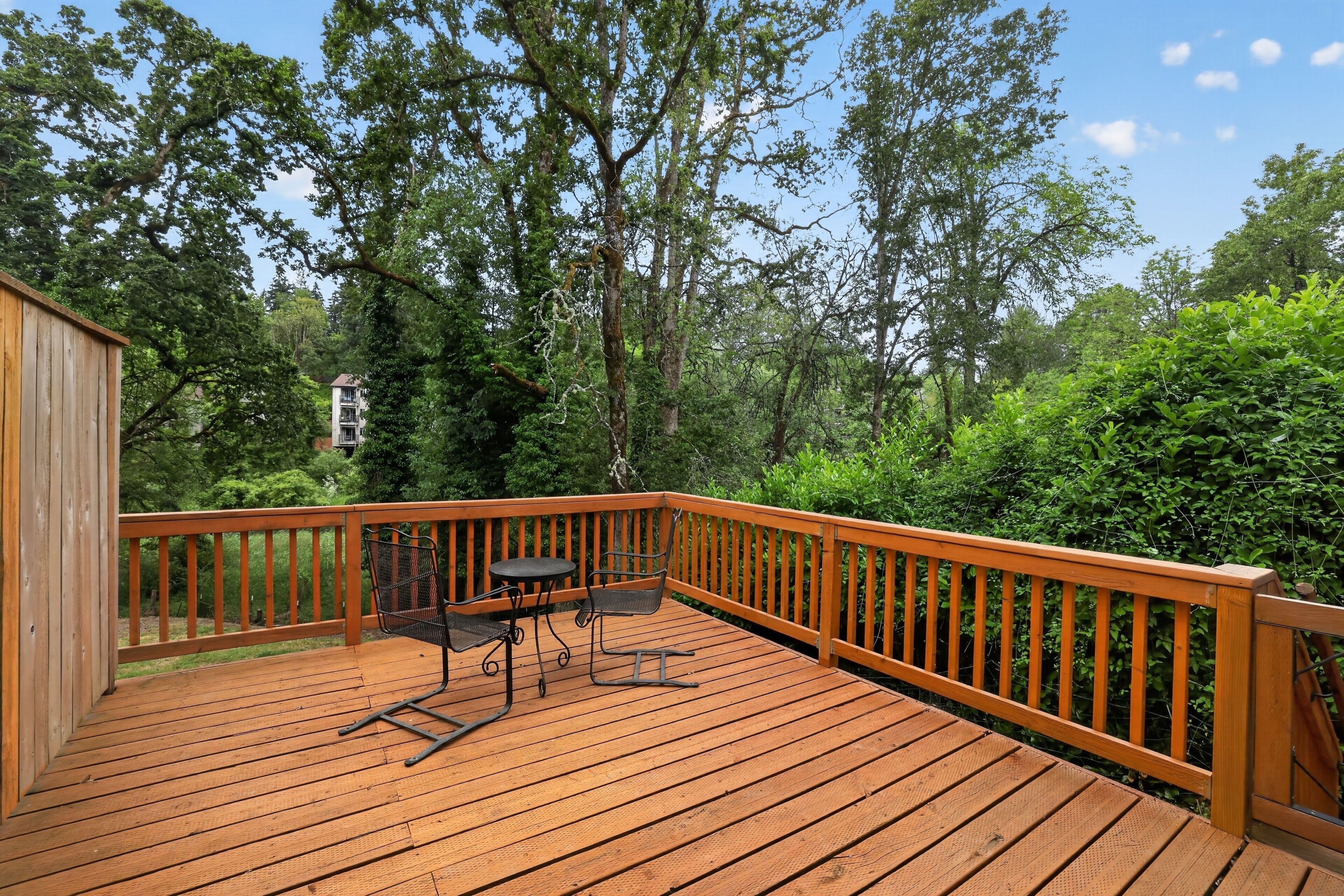 Eine Holzterrasse mit Tisch und Stühlen, umgeben von dichtem Grün und Bäumen.