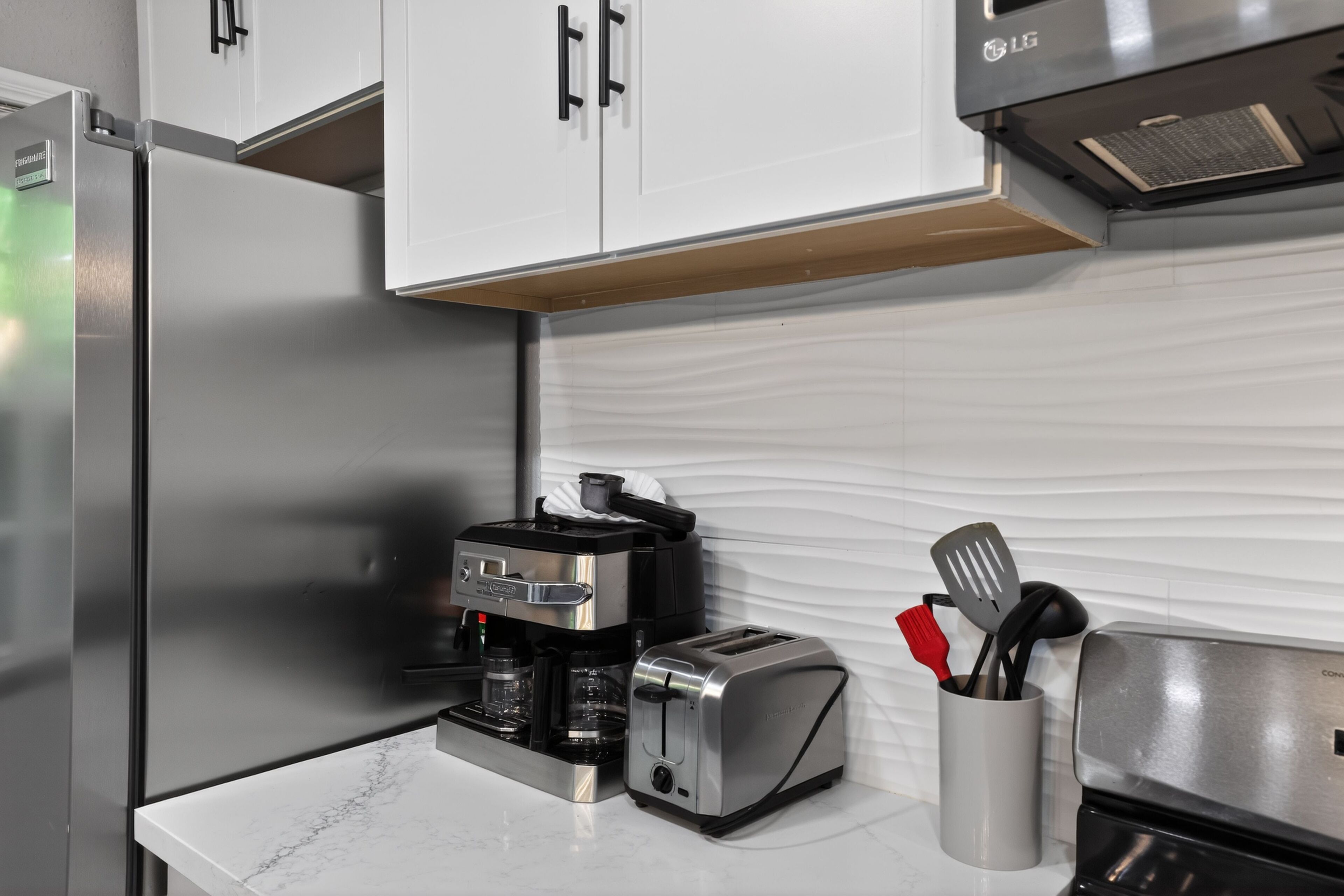 Una cocina con un refrigerador de acero inoxidable, una cafetera, un tostador y un recipiente para utensilios sobre la encimera.